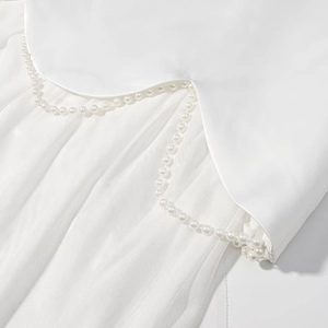 Detail of white satin dress featuring sheer mesh panel and elegant pearl bead chain trim