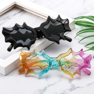 Close-up of black matte and colorful glitter bat-wing shaped sunglasses on marble