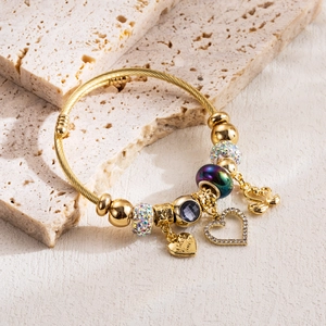 Dettaglio di un bracciale a perle dorate con ciondoli a cuore in cristallo e un cigno