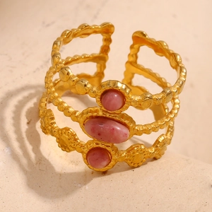 Drelagiger 18K vergoldeter offener Ring mit rosa Edelsteinen auf warmem Steinhintergrund