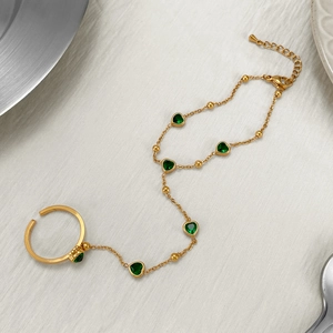 Gold stainless steel finger bracelet with green heart crystals on a metallic surface
