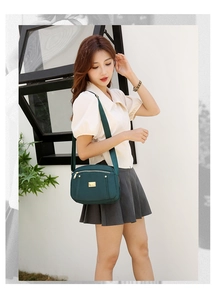 Deep green nylon crossbody bag styled on female model with cream blouse and grey skirt