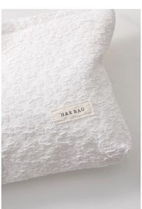 Detailed macro view of white canvas makeup bag featuring 3D floral embossed texture and logo