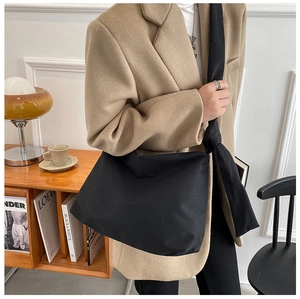 Detail of minimalist black canvas crossbody bag with decorative strap knots worn over shoulder