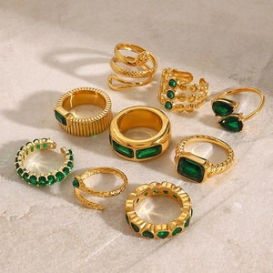 Detail view of nine gold stainless steel rings with green zircons on a stone background