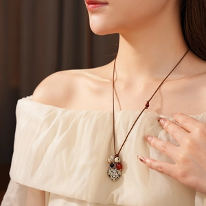Detail showing a heart-shaped stone pendant with a silver cross on a brown wax cord