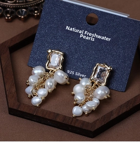 Detail of baroque pearl grape earrings with crystal studs on a dark wooden display tray