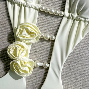 Detail view of cream swimsuit featuring 3D fabric roses and elegant pearl strap accents