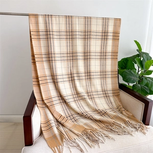 Detail of khaki plaid scarf with tassels draped on a wooden chair in a cozy setting
