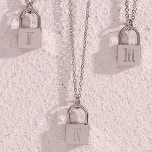Detailed close-up of three silver lock pendants with J, N, and M engravings on a wall
