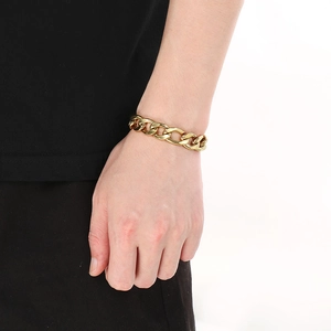 Close-up of a men's chunky gold-toned Cuban NK chain bracelet on a wrist over a white background