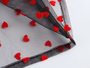 Close-up of sheer black mesh fabric featuring vibrant red flocked heart patterns