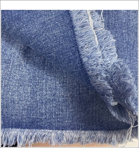Detailed close-up of blue denim fabric showing twill texture and distressed fringe edges