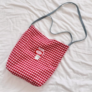 Detailed close-up of red and white plaid tote bag with decorative brand tag and gray strap