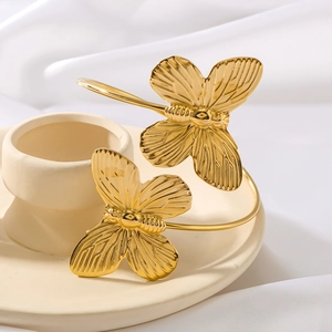 Polished gold butterfly open cuff bracelet with 3D wings on a white textile surface