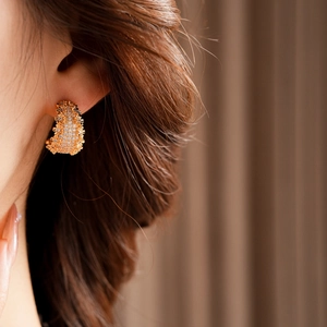 Détail de boucles d'oreilles C dorées élégantes avec zircons portées par un mannequin