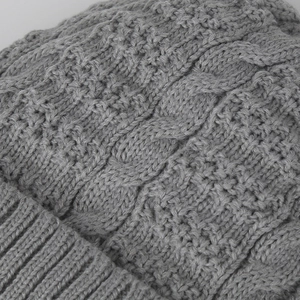 Macro shot of gray cable knit beanie showing thick texture and ribbed hem detail