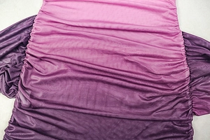 Dettaglio del tessuto a rete sfumato da rosa a viola con texture increspata sul vestito