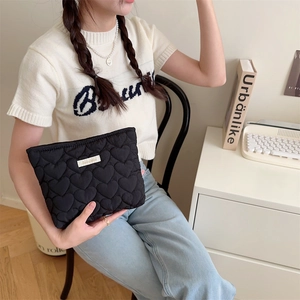 Dettaglio della pochette nera trapuntata a cuore tenuta da una modella in un set moderno