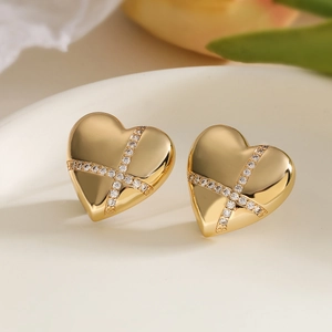 Golden heart-shaped stud earrings with sparkling zircon cross inlay on a white tray