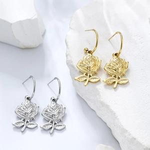 Detailed view of 3D rose flower earrings in gold and silver on stone background