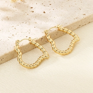 Detail of twisted gold heart hoop earrings on elegant beige stone and fabric background