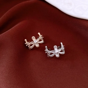 Detail van goud- en zilverkleurige strik-oorclips met zirkonen op rode stoffen achtergrond
