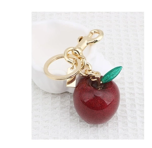 Detail shot of a sparkling red apple keychain with a green leaf on golden metal hardware