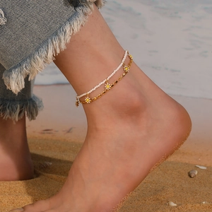 Close-up of double-layer stainless steel anklet with white beads and daisy charms on a beach