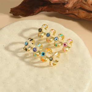 Set of eight gold open rings with colorful enamel evil eye patterns on ceramic plate