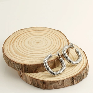Détail de créoles torsadées argentées à texture spirale sur fond de bois naturel
