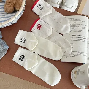 Detail of white cotton socks with cute puppy embroidery and red ribbed edges on wood