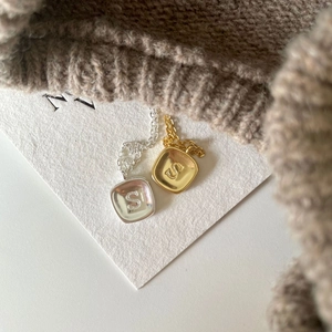 Detailed view of vintage gold and silver S-letter square pendant necklaces on white card
