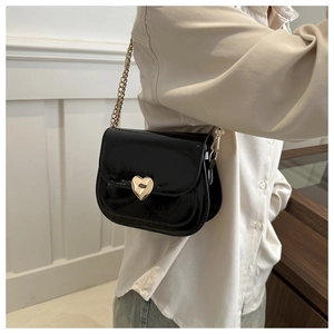 Detail of black patent leather crossbody bag with gold heart clasp and chain strap