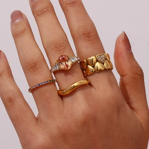 Detail of gold-plated rings set featuring pear-cut pink zircon and wavy band stack