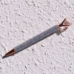Close-up of rose gold crystal ballpoint pen with colorful rhinestones on a textured surface
