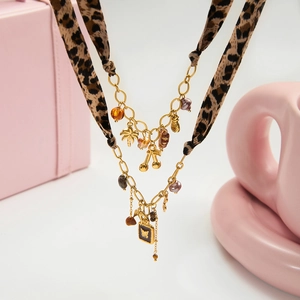 Détail d'un collier multicouche avec ruban léopard et breloques dorées tropicales