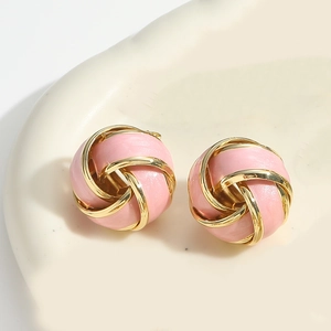Detail of pink enamel and gold knot vortex earrings on a warm ceramic background
