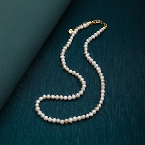 Detail of natural freshwater pearl necklace with gold clasp and brand tag on textured surface