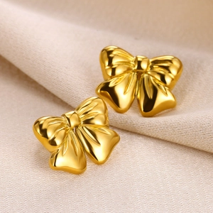 Macro detail of polished 18K gold butterfly bow earrings on soft knitted fabric