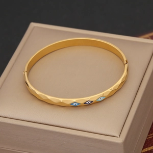 Golden stainless steel evil eye bangle featuring faceted texture on a leather box