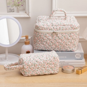 Quilted floral makeup bag set with top handle and zippers on a wooden vanity table