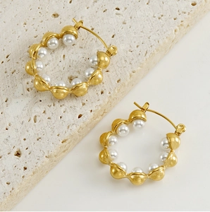 Detailed macro view of 18k gold earrings with inlaid pearls on a stone surface