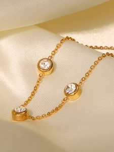 Détail d'une chaîne plaquée or 18K avec cristaux ronds posée sur de la soie champagne