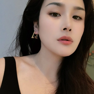 Close-up of model wearing geometric black enamel flower earrings with gold finish details