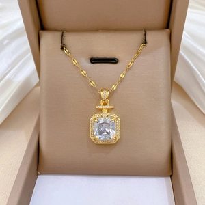 Détail du collier bouteille de parfum dorée avec zircon carré sur fond en soie de luxe