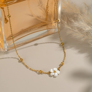 Detail view of 18K gold plated necklace with white shell flower pendant on perfume bottle