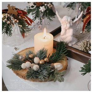 Close-up of a lit candle on wood base with pine branches and golden Christmas berries
