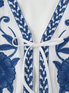 Detailed embroidery on white V-neck top with floral patterns and bow tie closure