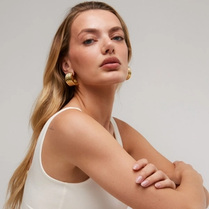 Detail of 18K gold-plated twisted hoop earrings worn by a model in a fashion studio